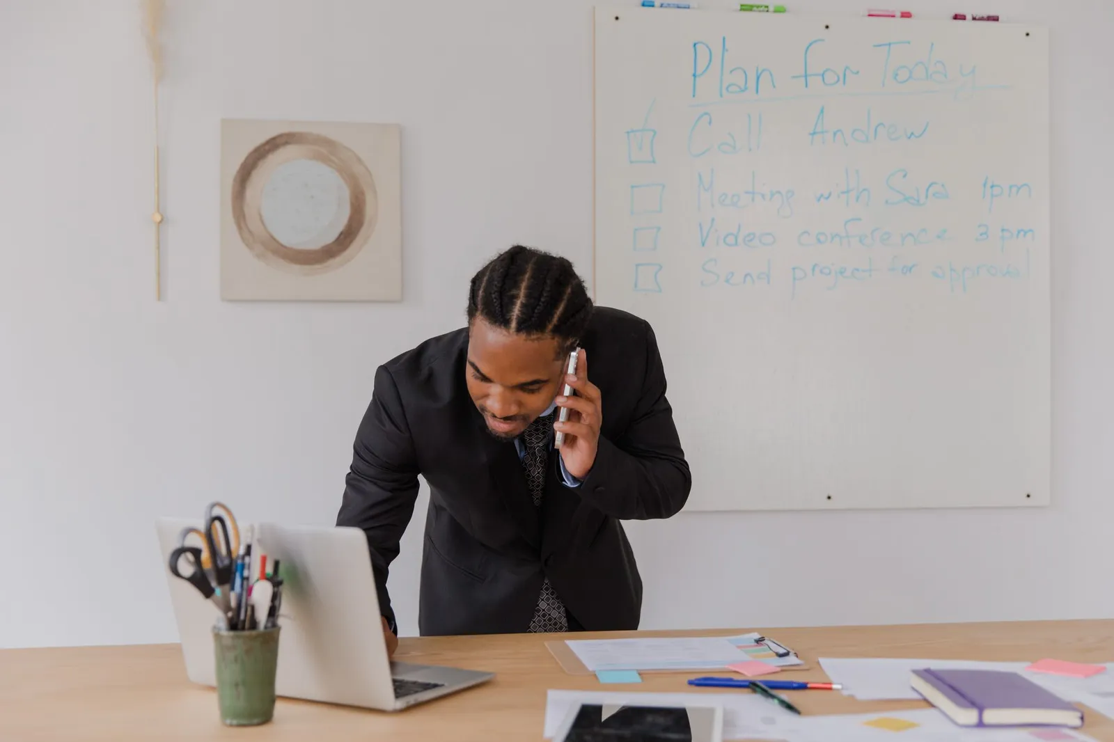 An owner on a call at his desk, the plan for the day on the board behind him