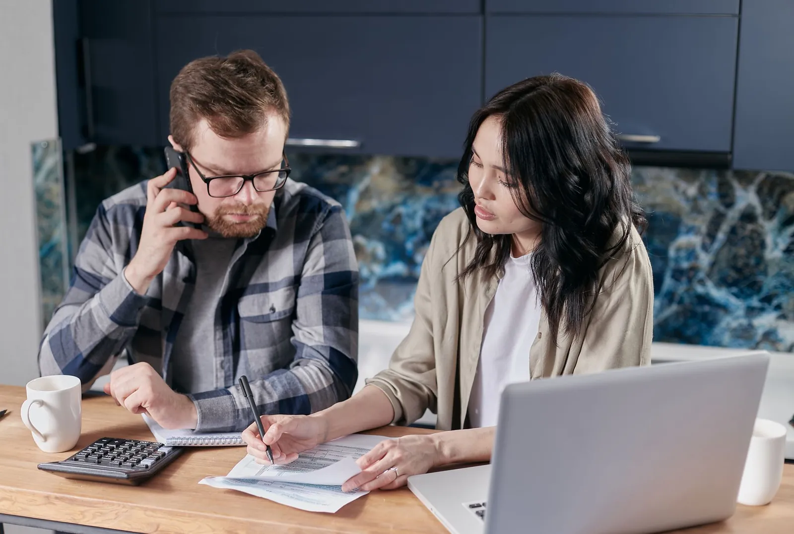 A couple at their kitchen table going through the numbers, one of them on a call