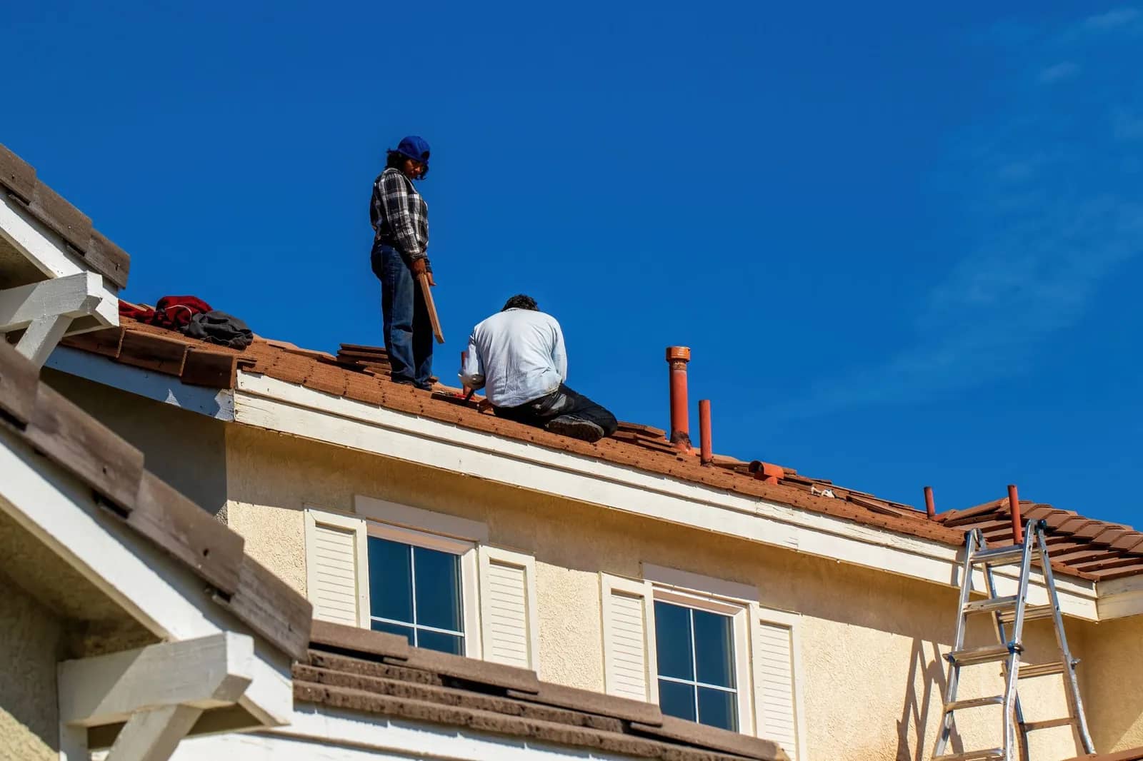 A roofer at work on a tiled roof under a blue sky