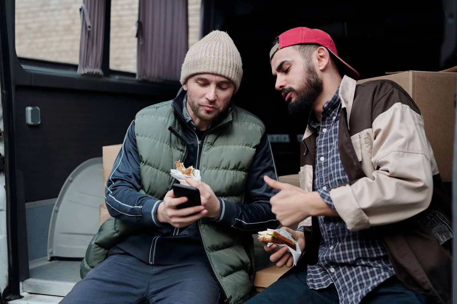 Dos trabajadores descansando en la parte de atrás de su camioneta, uno revisando su teléfono