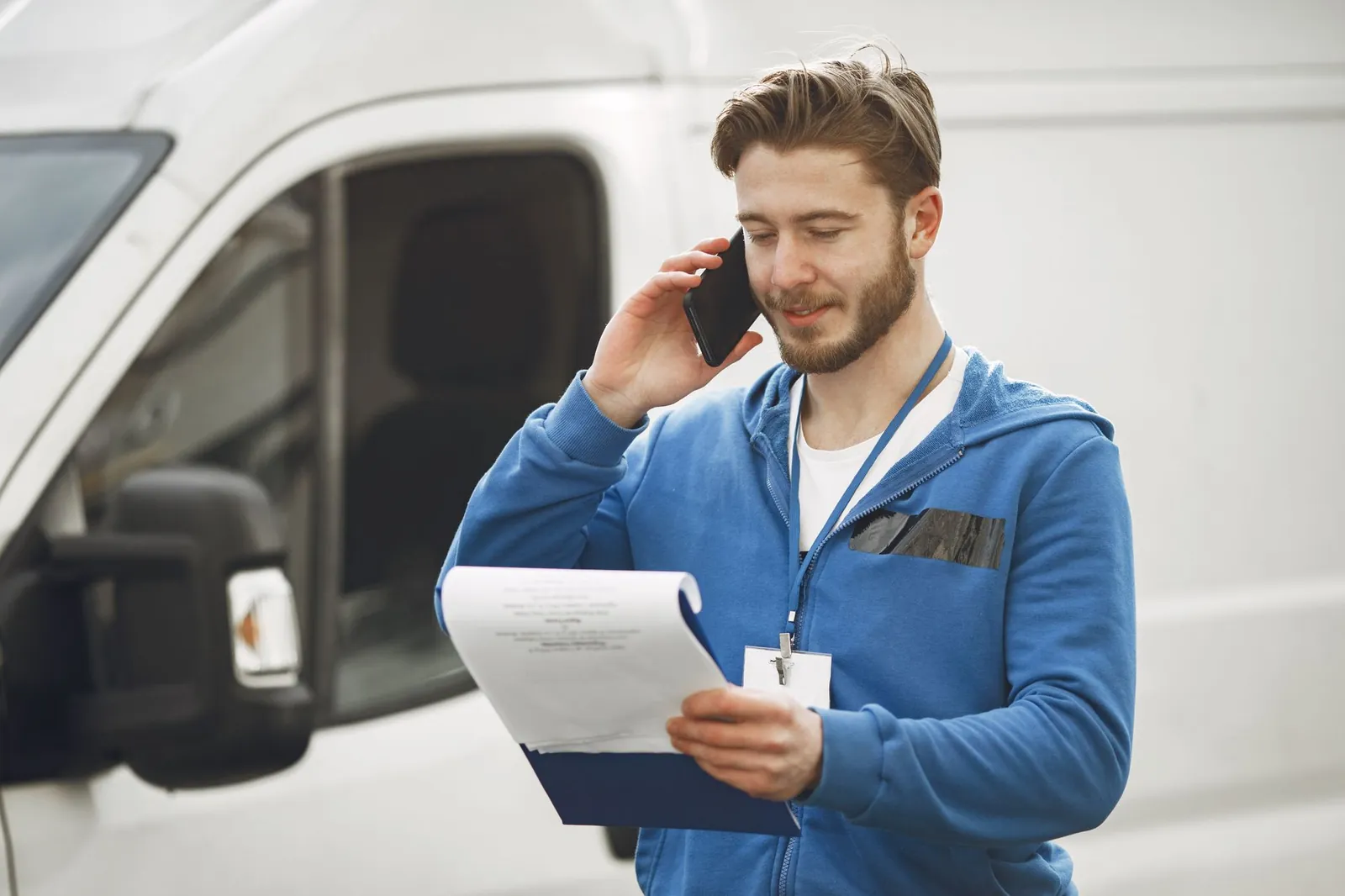Un técnico junto a su camioneta, hablando por teléfono con un portapapeles en la mano