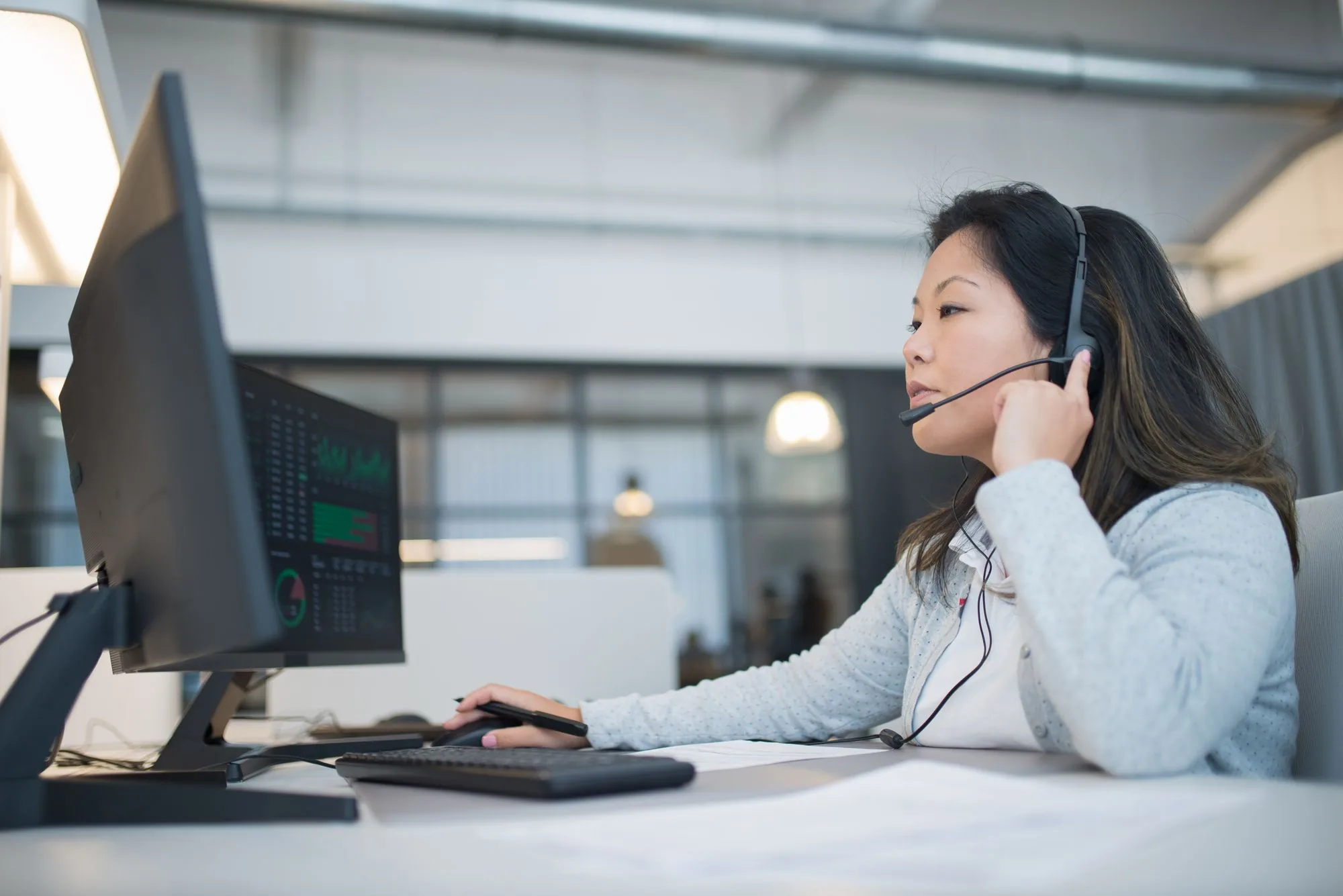 Una mujer con auriculares y micrófono trabajando en un escritorio con dos monitores